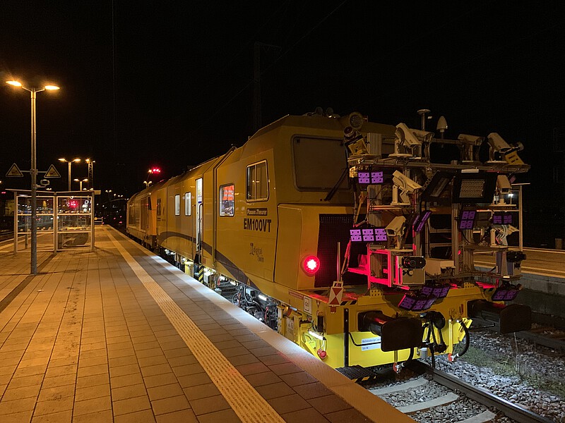 Gelbes Messfahrzeug nachts im Einsatz. Das Gleis wird beleuchtet und mithilfe von Infrarotlampen und Kameras erfasst.